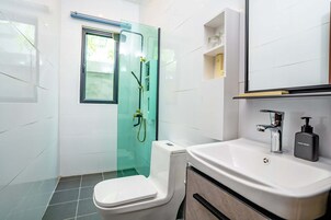 Un baño moderno con cabina de ducha de vidrio, inodoro blanco, lavabo con dispensador de jabón y espejo sobre el lavabo.