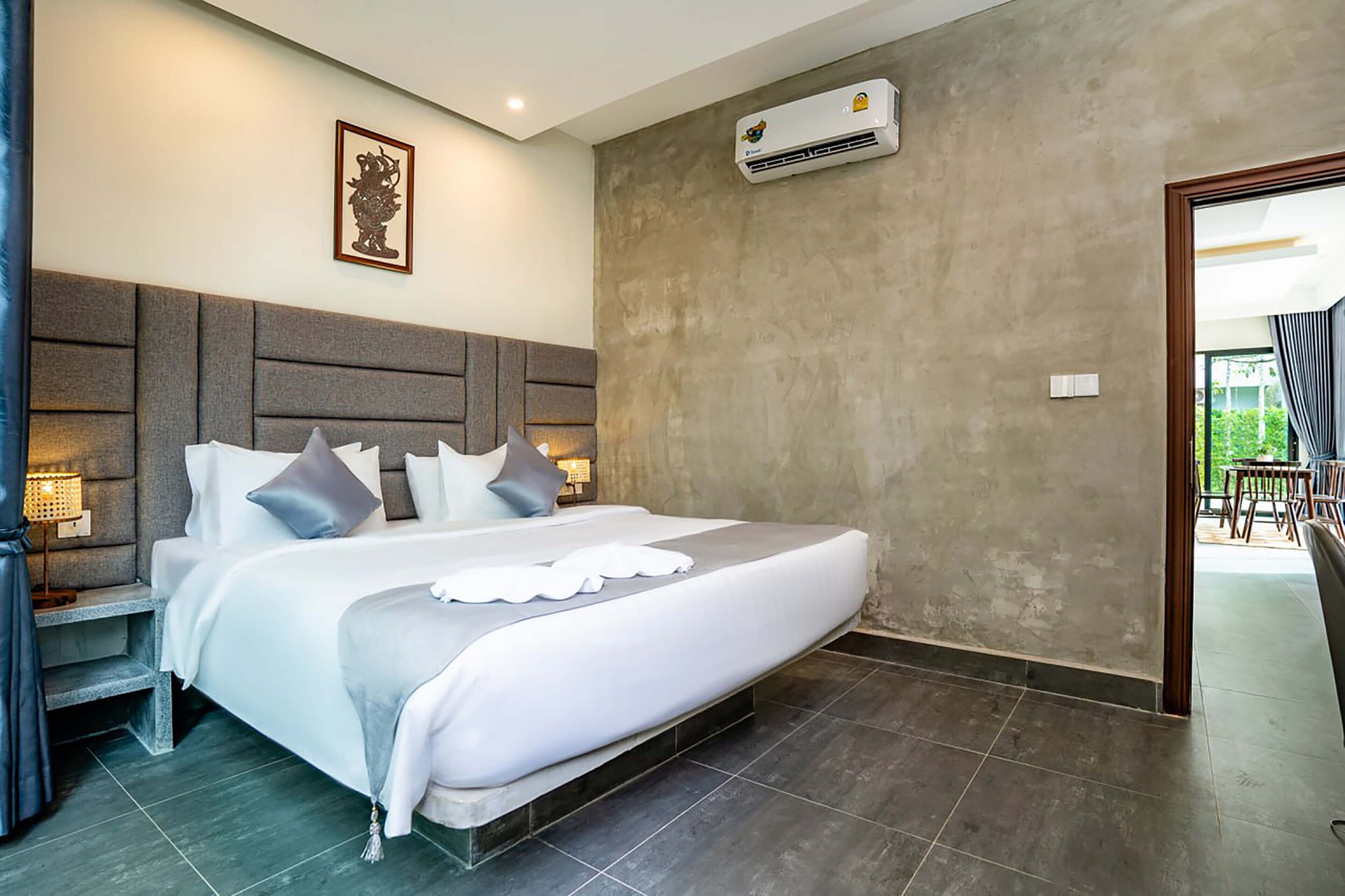 Habitación de hotel moderna con una cama grande, cabecera gris, lámparas de noche y vistas al exterior.