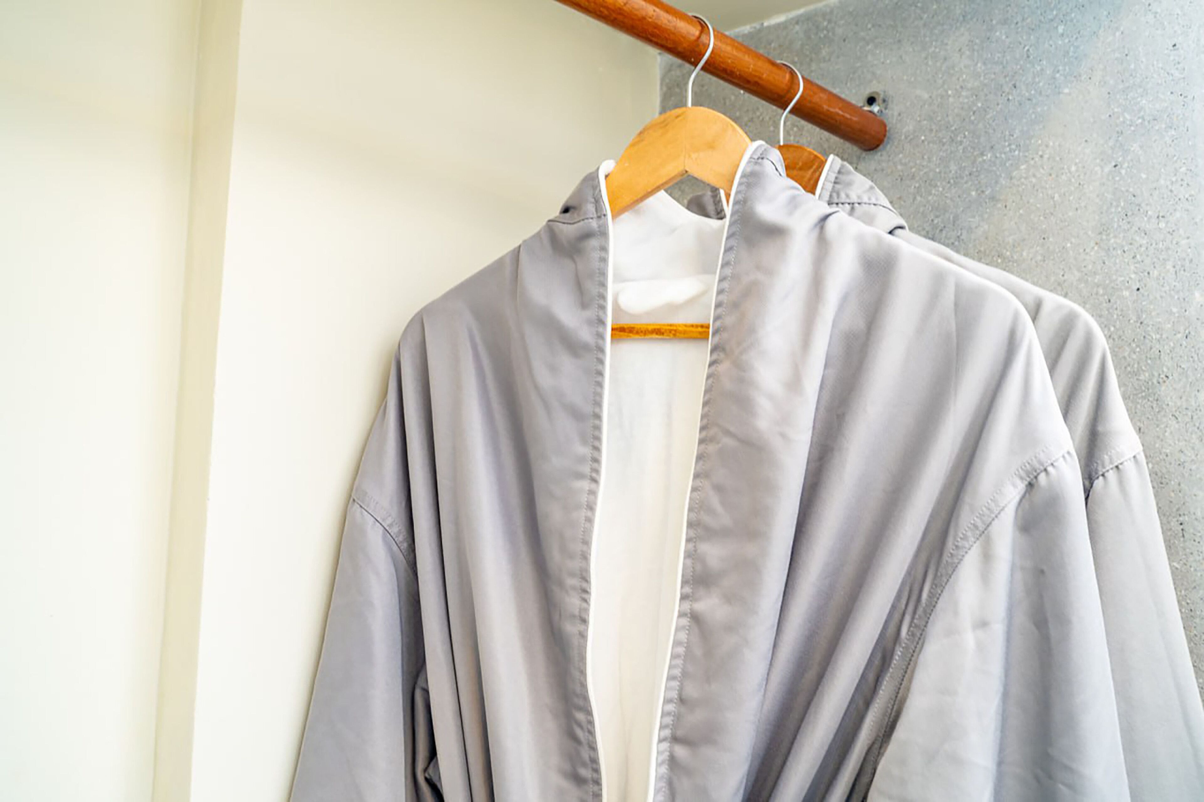 Una camisa gris colgada de una percha de madera frente a una pared lisa.