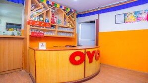 A reception desk with a wooden finish and a red logo. Behind the desk, there are shelves with various items and a colorful decoration.