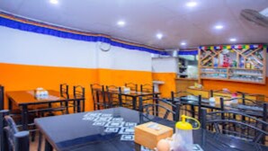 A restaurant interior with tables and chairs, a clock on the wall, and a colorful decoration above the counter.