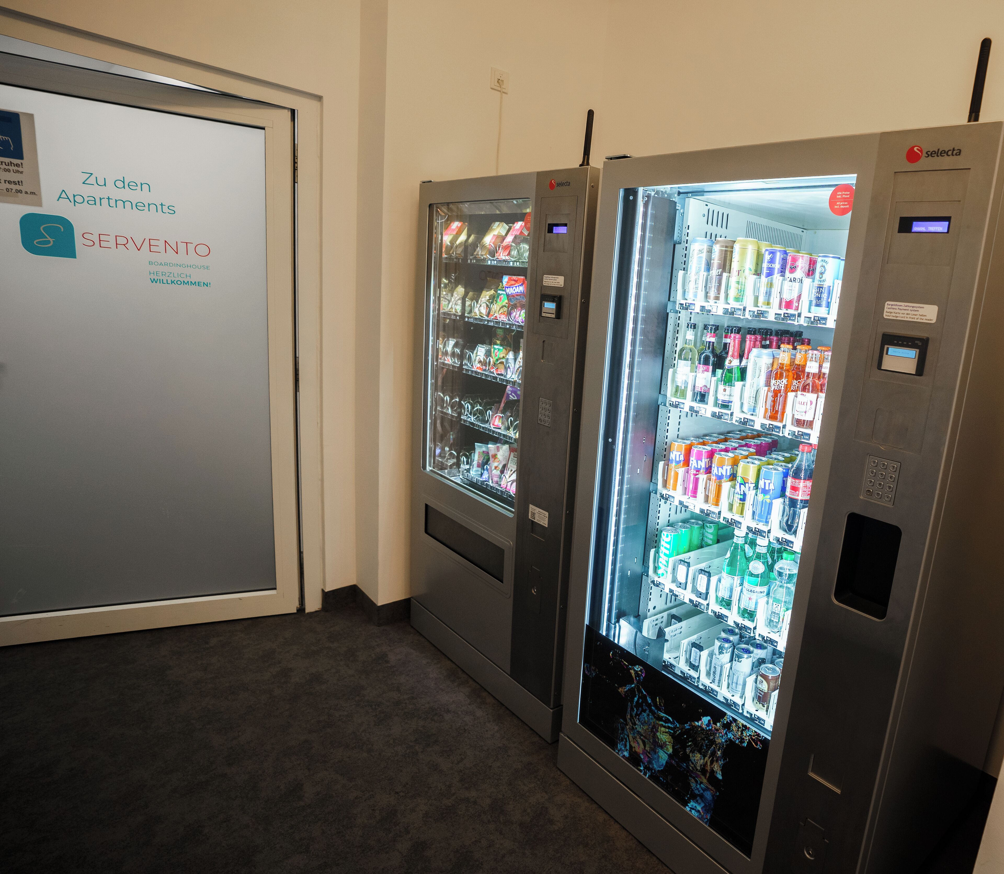 Two self-service beverage vending machines in a hallway.