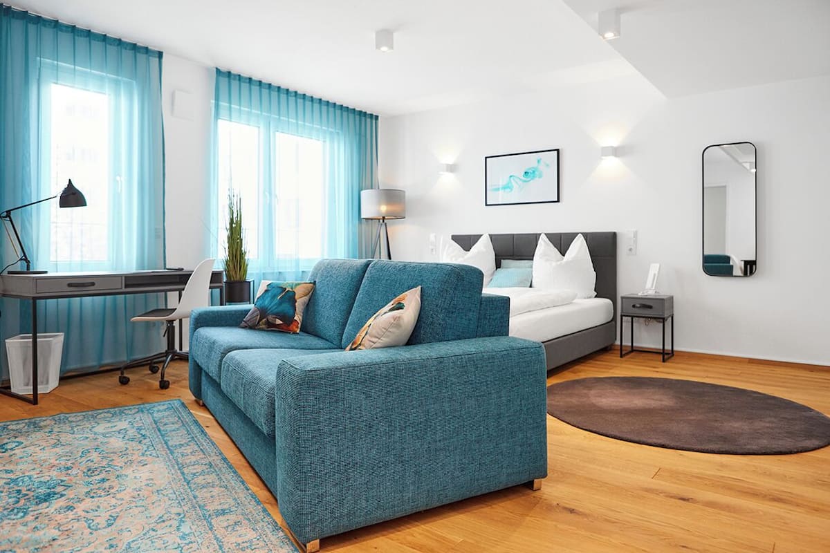 Un dormitorio moderno con un sofá azul, una cama, un escritorio y un espejo grande.