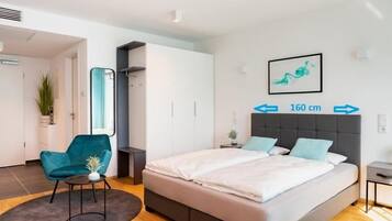Une chambre à coucher moderne avec un lit, une chaise et un miroir. Le mur est blanc et orné d’un tableau encadré.