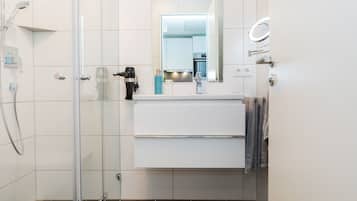 A modern bathroom with a glass shower enclosure, a white sink, and a mirror with a light.