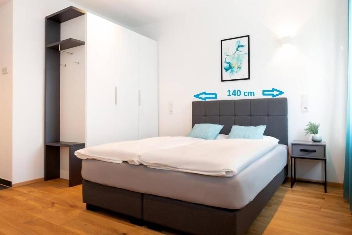 Un dormitorio con cama, mesita de noche, estante en la pared y una obra de arte enmarcada.