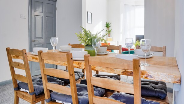 A dining area with a wooden table, chairs with cushions, and a vase with plants.