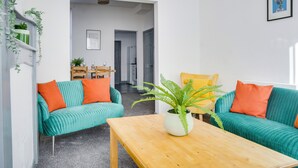 A modern living room with teal sofas, a wooden coffee table, and a potted fern.