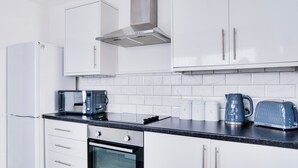 A modern kitchen with white cabinets, a stainless steel range hood, a built-in oven, a microwave, a kettle, and a toaster.