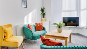 A modern living room with a yellow armchair, teal sofa, and a wooden coffee table.