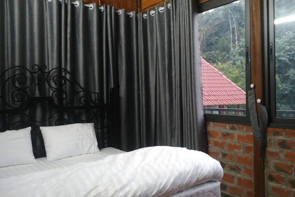 A bed with white bedding, a black metal headboard, and a view of a red-roofed building through a window.