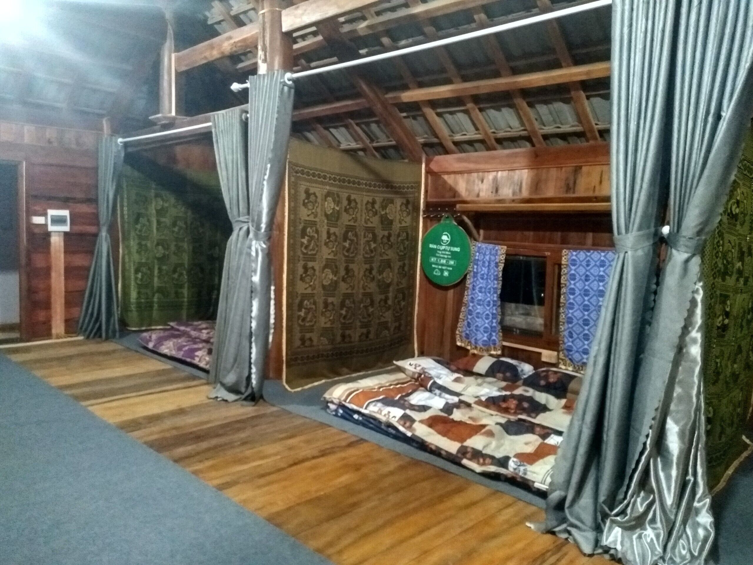 Una habitación con techo de madera, cama con ropa de cama estampada, cortinas y un letrero verde en la pared.
