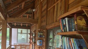 A wooden cabin with a wooden deck, bookshelves, and a person sitting on the deck. - Farmstay Ban Bua (Moc Son)