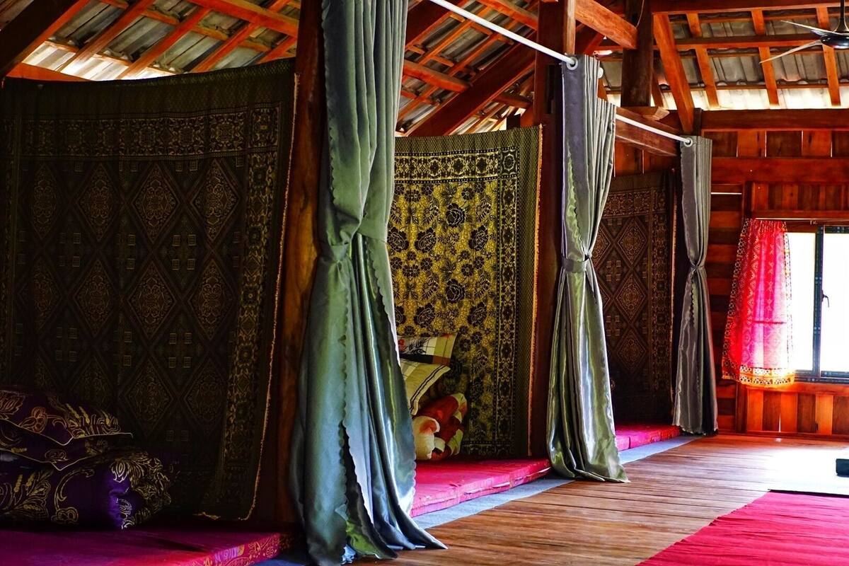 A room with a wooden ceiling, a bed with a red mattress, and a window with a red curtain.