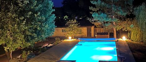 Ein rechteckiger Pool mit Fliesen umgeben von Bäumen und einem Gebäude mit einem geflasterten Dach.