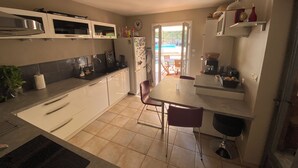 Cozinha compacta com armários brancos, uma mesa de jantar e uma cafeteira.