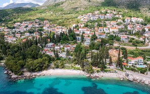 A coastal residential area with houses on a hillside, a beach, and clear turquoise waters.