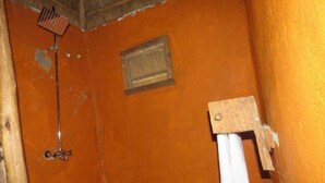 Ein Badezimmer mit orangefarbener Wand, einem Holzbodenregal, einer Duschbrause und einem Handtuchhalter.