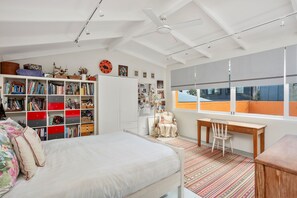 Een slaapkamer met een bed, een bureau, een stoel, een boekenkast en een raam.