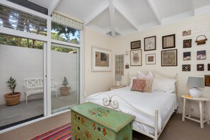Ein Schlafzimmer mit Bett, Kommode, Nachttisch, Fenster mit Jalousien und Bildern an der Wand.