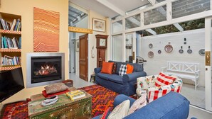 A living room with a fireplace, a sofa, a television, and a bookshelf. - Characterful 4BR home w/ pool, full of artwork w/ galleries close by (Paddington)