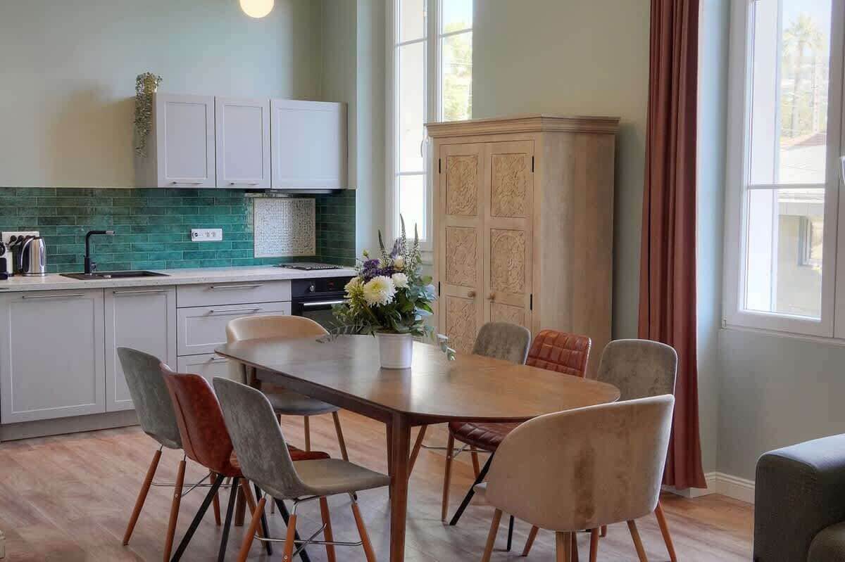 Una cocina moderna con armarios blancos, salpicadero verde y un comedor con mesa y sillas de madera.