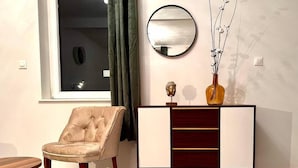 Un soggiorno moderno con una poltrona beige, un tavolino in legno, un mobile contenitore in legno chiaro e scuro con soprammobili e uno specchio rotondo appeso al muro.