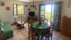 Un comedor con una mesa dispuesta para cuatro, un televisor sobre un mueble y vistas al exterior a través de una ventana.