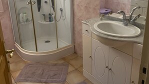 Un baño con ducha envuelta en vidrio, lavabo con espejo y tocador con armarios.