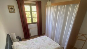 Un dormitorio con cama, mesita de noche, lámpara, ventana con cortinas y radiador.