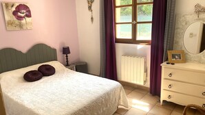 Un dormitorio con cama, cómoda, espejo, radiador y ventana con cortinas.