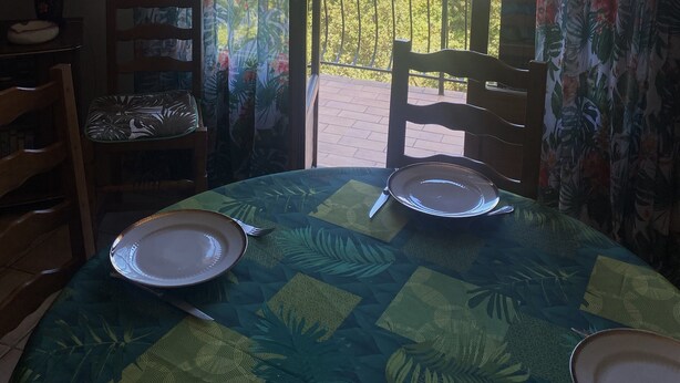 Un comedor con una mesa preparada para dos personas, sillas y vistas a un paisaje montañoso desde un balcón.