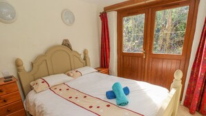 Una cama bien hecha con una colcha blanca y beige, un cabecero de madera y una ventana con cortinas.