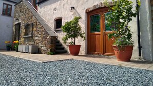Una escalera de piedra que lleva a una puerta de madera con un ventanal de vidrio verde, rodeada de plantas en macetas y un camino de grava.