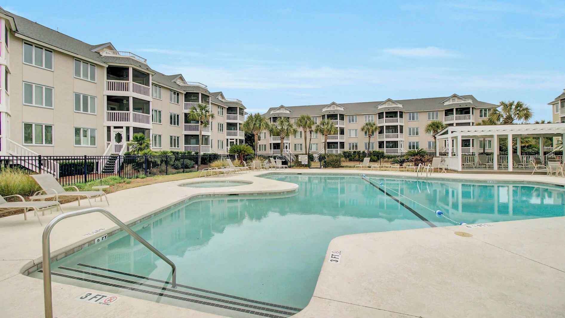 A swimming pool with a 3 FT depth marker, surrounded by multi-story buildings with balconies and palm trees.