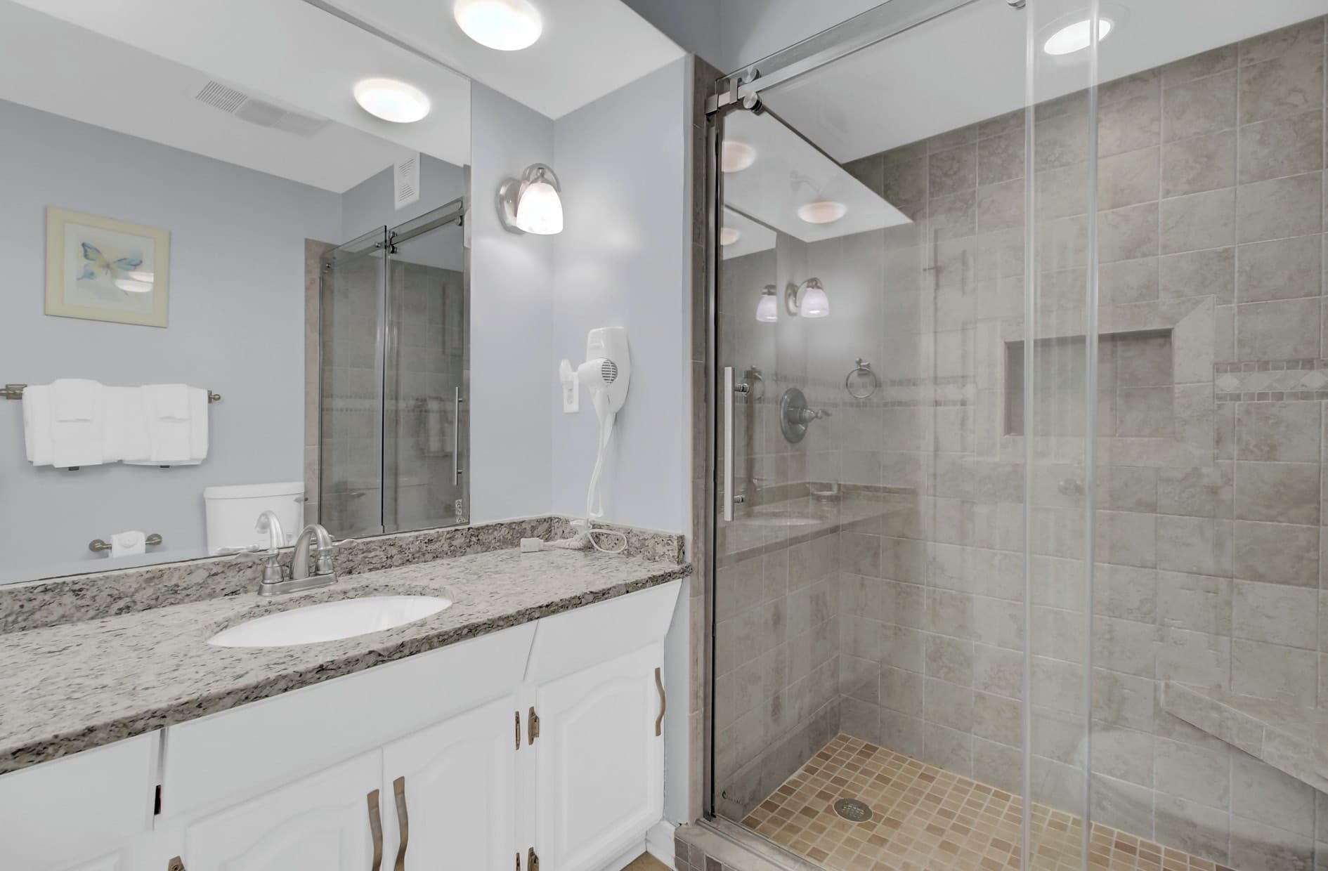 Un baño moderno con cabina de ducha de vidrio, lavabo blanco y encimera de mármol.