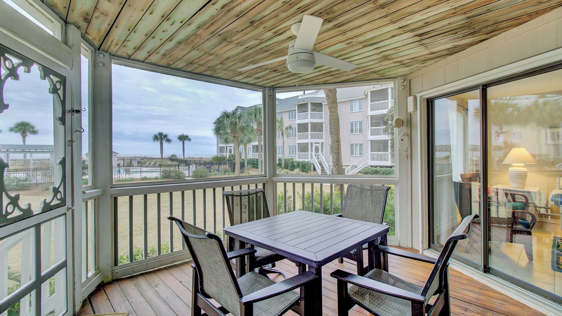 A covered outdoor area with a table and chairs, a ceiling fan, and a view of a residential building.