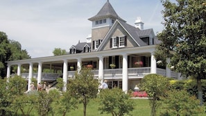 A large, two-story house with a wrap-around porch, multiple windows, and a tower-like structure.