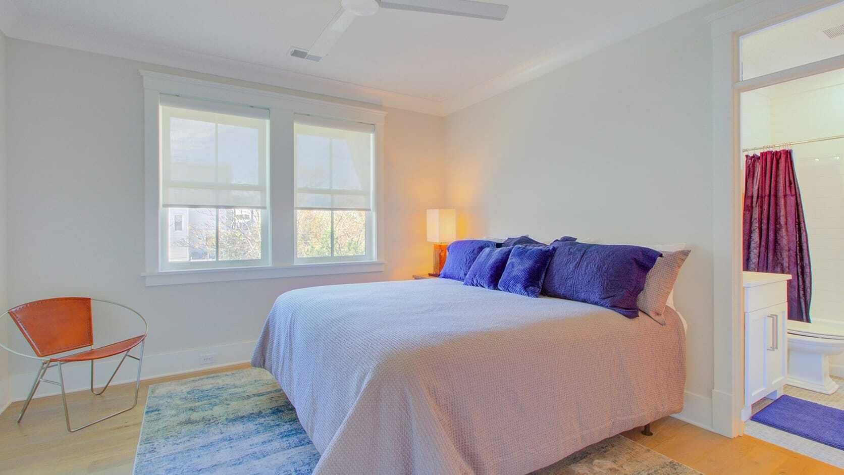 A bedroom with a bed, a chair, a window, and a bathroom.