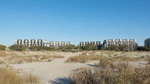 A beachfront hotel with multiple buildings, a sandy path, and sparse vegetation. - 322 D Shipwatch by Avantstay Community Pool Access & Close to Beach! (Isle of Palms)