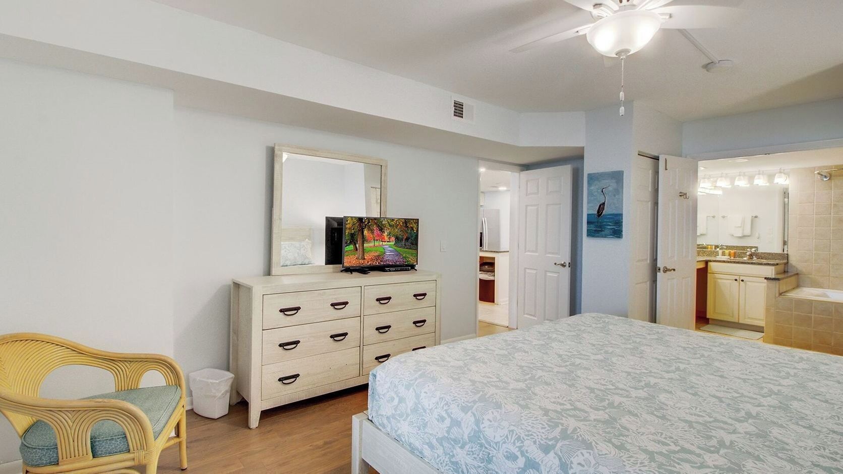 A bedroom with a bed, dresser, chair, and a bathroom visible through an open door.