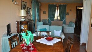 A dining area with a wooden table, chairs, a red bowl, and a white tablecloth.