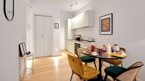 Une cuisine compacte dotée d’appareils électroménagers modernes, un coin repas avec une table ronde et des chaises, et une œuvre d’art encadrée accrochée au mur.