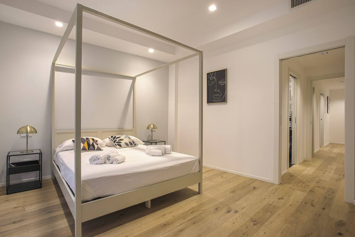 Ein modernes Schlafzimmer mit einem Himmelbett, einem Nachttisch mit Lampe und einem gerahmten Kunstwerk an der Wand.