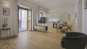Un vaste espace de vie doté d’un plancher en bois, d’une table à manger avec des chaises, d’un coin cuisine avec des placards et d’un grand téléviseur à écran plat fixé au mur.