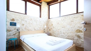 Ein Schlafzimmer mit Steinwand, einem hölzernen Bettgestell, einem kleinen Tisch mit Stuhl und einem Fenster mit Holzbalken.