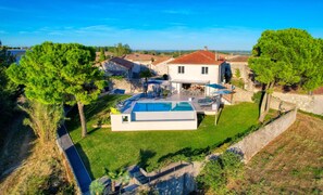 A modern villa with a swimming pool, outdoor seating, and a stone wall.