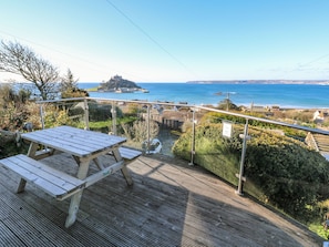 Una terraza de madera con una mesa de picnic que da a vistas de la costa, incluyendo una isla distante y el mar.