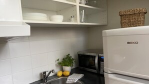 A kitchen with a sink, a microwave, a refrigerator, and a shelf with dishes and a plant. - Charming Apartment in the Heart of Stockholm! (Stockholm)