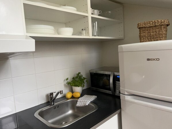A kitchen with a sink, a microwave, a refrigerator, and a shelf with dishes and a plant. - Charming Apartment in the Heart of Stockholm! (Stockholm)